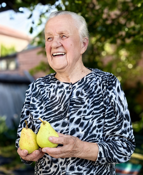 Eine lächelnde alte Frau hält zwei Birnen in der Hand.